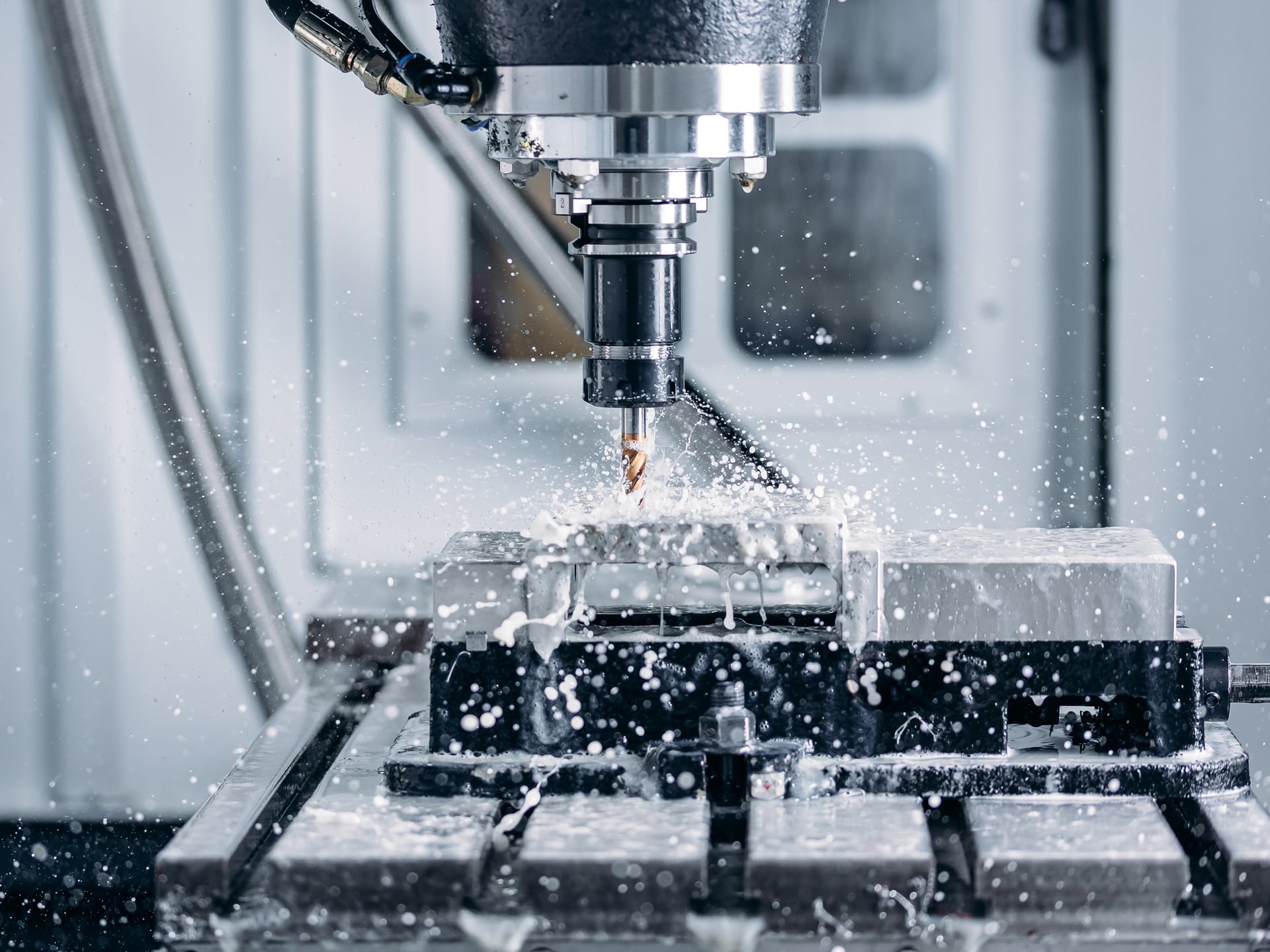 Close-up of a CNC milling machine cutting metal, coolant spraying and metal shavings flying around the spinning tool in a workshop.