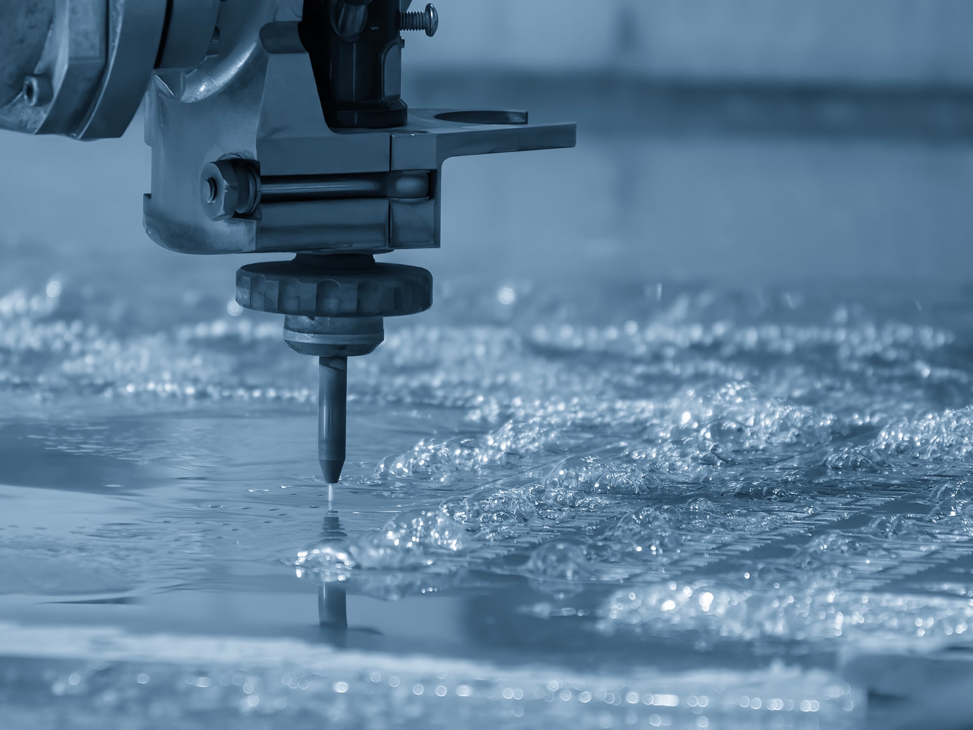 Close-up of a waterjet cutting machine slicing metal, water spraying and bubbles forming at the cut. Image tinted blue.