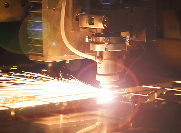 Close-up of a CNC laser cutting machine in use, bright sparks flying as it cuts metal in an industrial workshop setting.