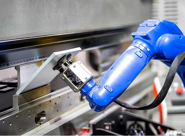 A blue industrial robotic arm operates a metal sheet bending machine, precisely shaping a metal piece in a modern factory setting.